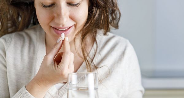 Eine junge Frau nimmt eine Tablette mit einem Glas Wasser ein. 