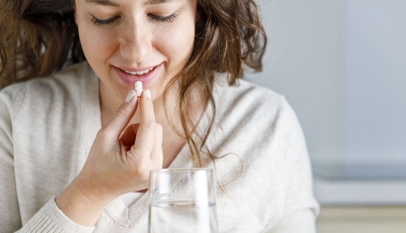 Eine junge Frau nimmt eine Tablette mit einem Glas Wasser ein.