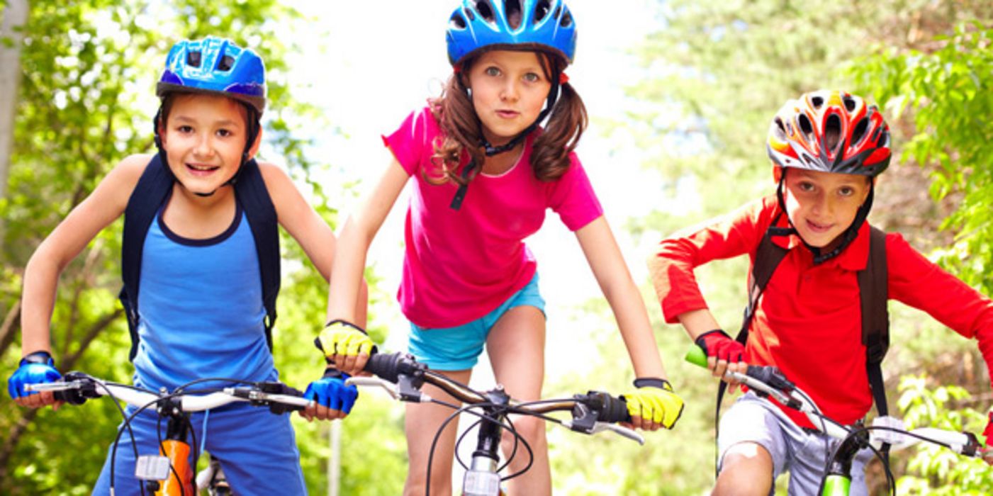 Drei Kinder mit Fahrradhelmen radeln auf einem Weg auf die Kamera zu