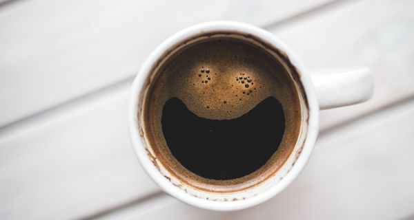 Schwarzer Kaffee mit einem lächelnden Gesicht als Schaum.