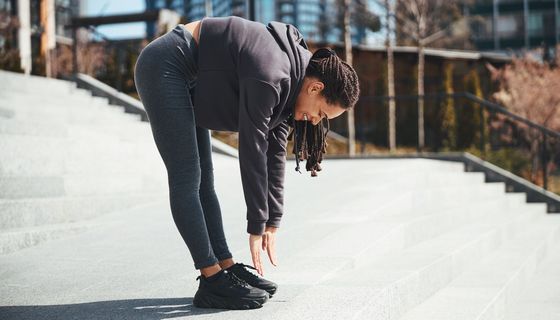 Eine Frau macht draußen eine Vorwärtsbeuge: Sie drückt die Knie durch und versucht, mit den Fingerspitzen die Zehen zu berühren. 