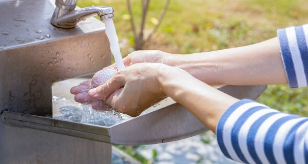 Eine Person wäscht sich die Hände an einem sauberen Außenwaschbecken im Freien. 