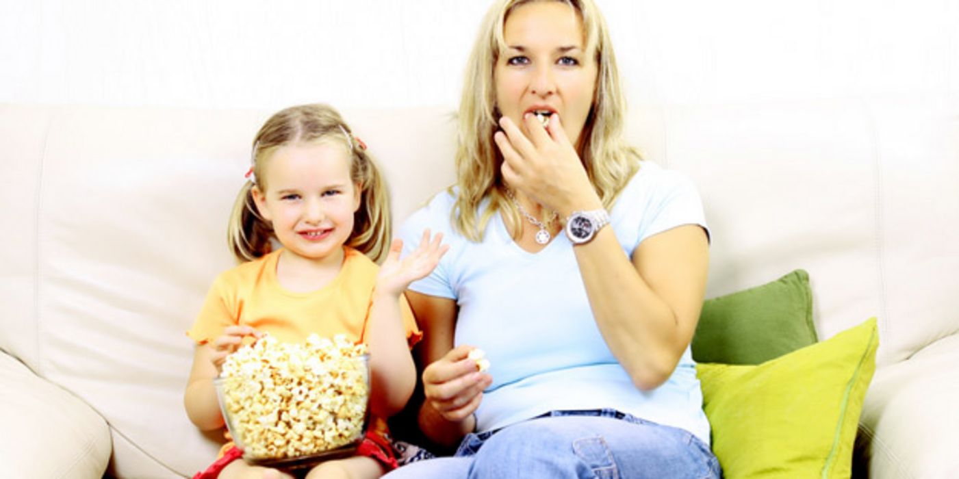 Mutter und Tochter sitzen auf der Couch und essen Popcorn