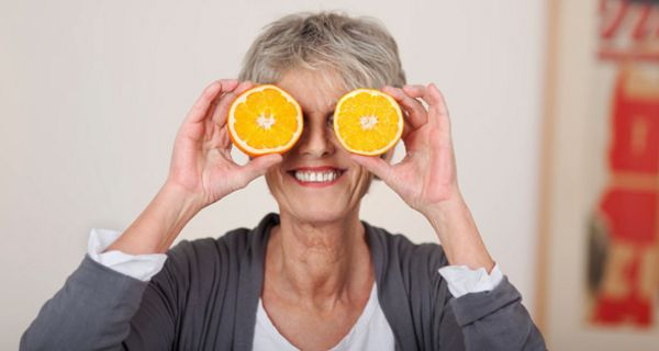 Ältere Frau hält sich Orangenhälften vor die Augen.
