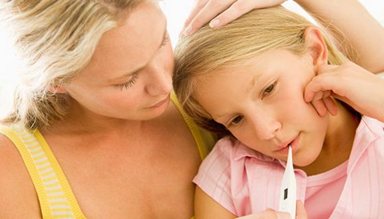 Mutter misst bei Schulkind (Mädchen, ca. 9 Jahre) Fieber und stützt mit einer Hand ihren Kopf. Beide sind blond.