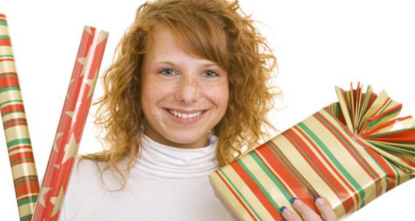 Rothaarige junge Frau mit Geschenkpapier und einem verpackten Geschenk in den Händen