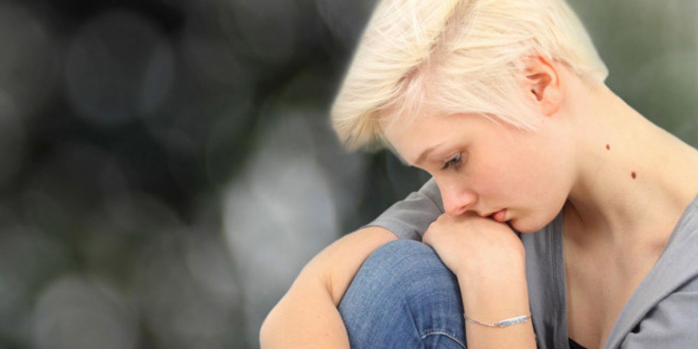 Junge blonde Frau schaut nachdenklich und stützt den Kopf auf ihr Knie.