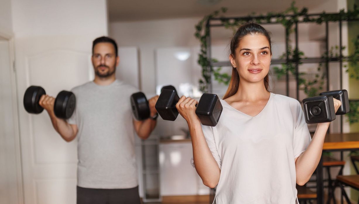 Ein Paar macht Hantelübungen zuhause.