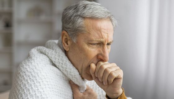 Ein älterer Mann hustet, eingewickelt in eine Decke.