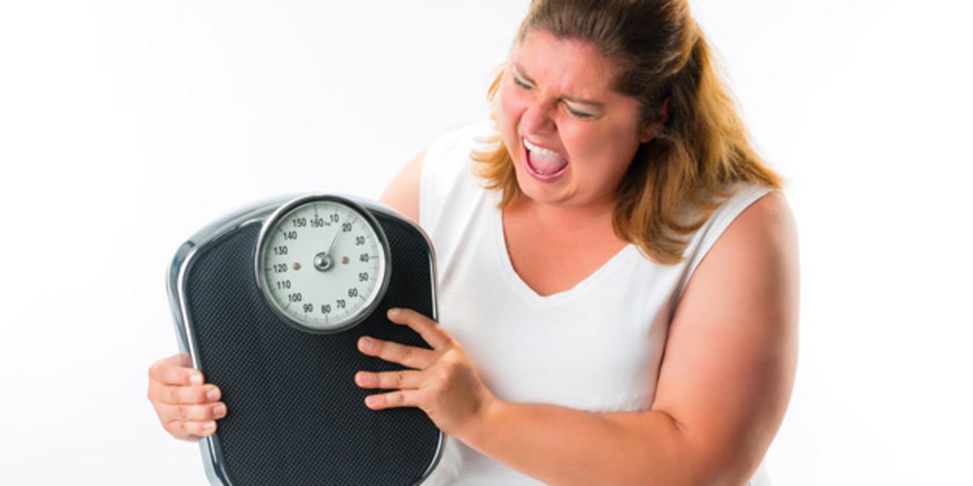 Übergewichtige Frau schüttelt zornig eine Waage