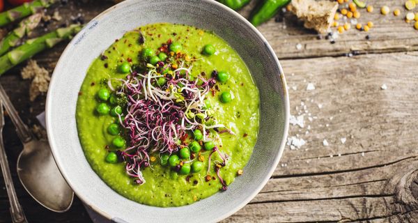 Foto von grüner Erbsensuppe in einem Teller, angerichtet mit Sprossen.