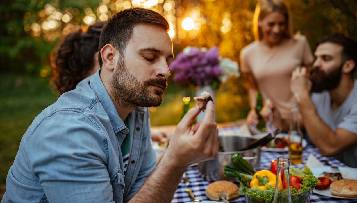 Mann, sitzt bei einer Grillparty und isst ein Stück Fleisch.