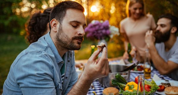 Mann, sitzt bei einer Grillparty und isst ein Stück Fleisch.