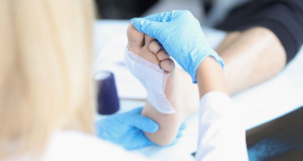 Eine pflegende Person kontrolliert die Wundauflage am Fuß einer Patientin.