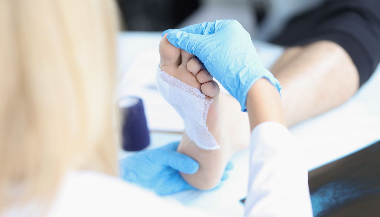 Eine pflegende Person kontrolliert die Wundauflage am Fuß einer Patientin.