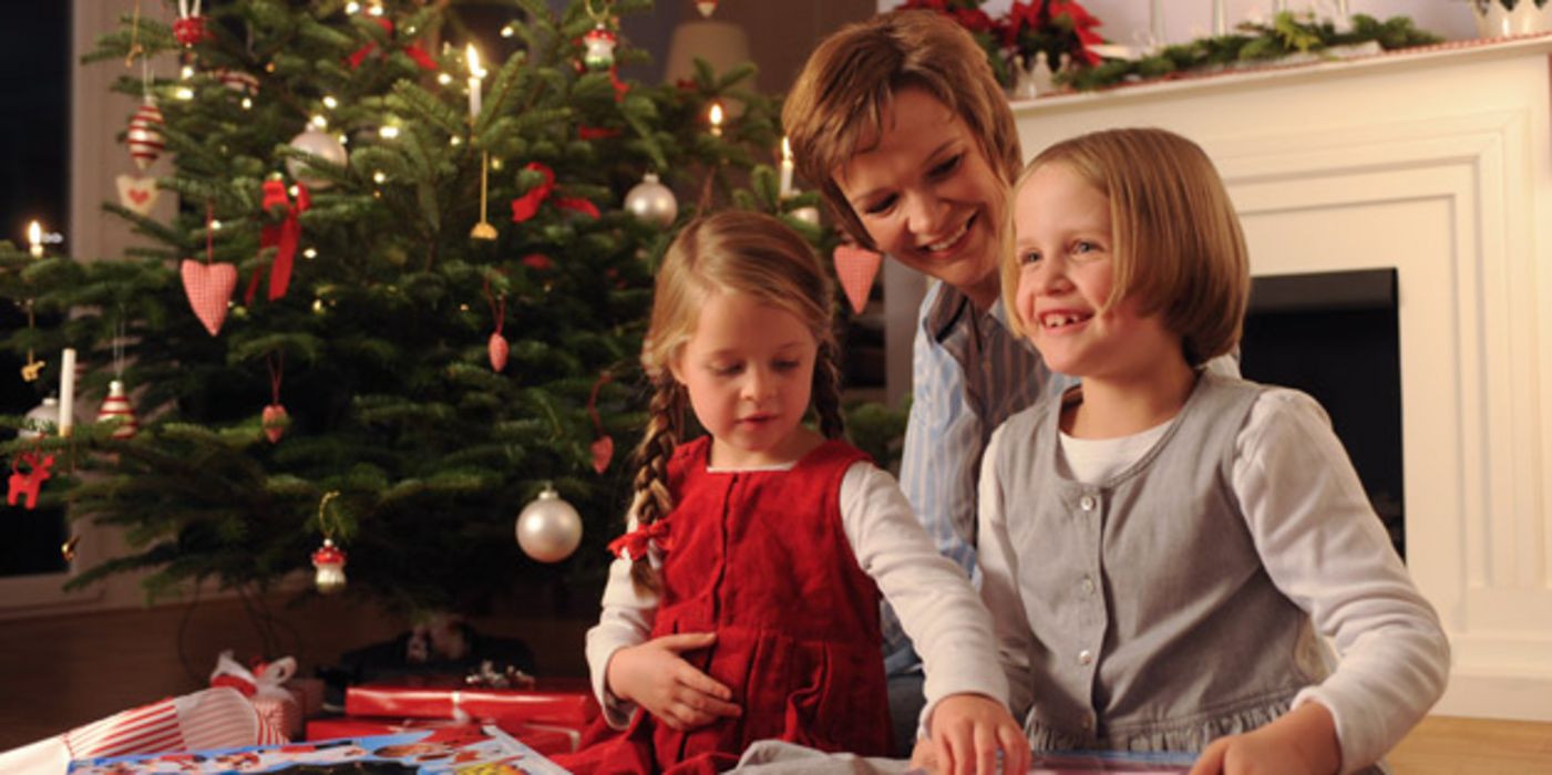 Eine Mutter und ihre zwei jungen Töchtern packen unter dem Christbaum Geschenke aus