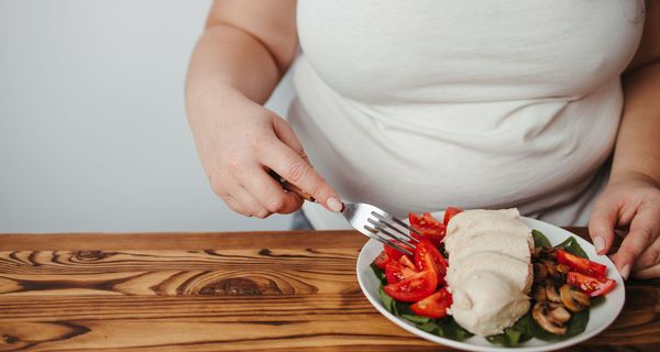 Übergewichtige Frau, isst einen Salat mit Mozzarella.