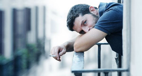 Rauchender Mann beugt sich über ein Balkongitter.