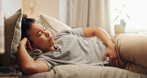 Frau hält sich den Unterbauch und liegt im Bett. Sie wirkt angespannt.