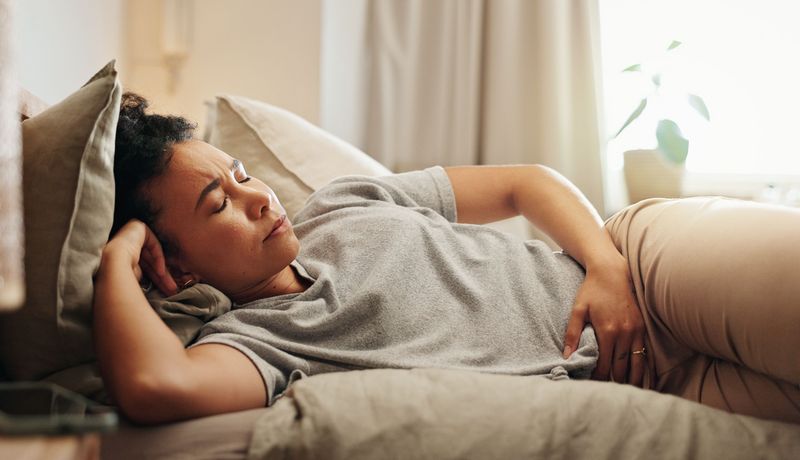 Frau hält sich den Unterbauch und liegt im Bett. Sie wirkt angespannt.