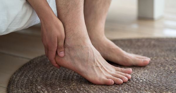 Fuße neben einem Bett, die Hand fasst unter die Ferse.