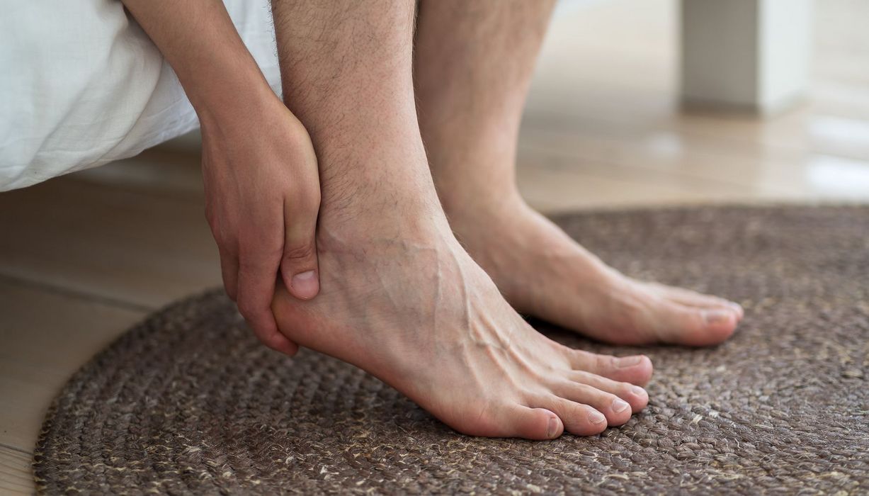 Fuße neben einem Bett, die Hand fasst unter die Ferse.