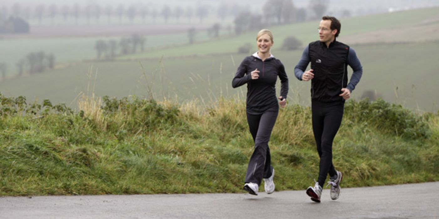 Mann und Frau joggen bei trübem Wetter über ein Feld