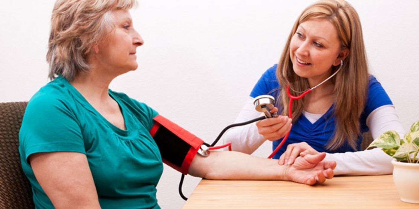Frau um die 50 bekommt von Pflegerin den Blutdruck gemessen