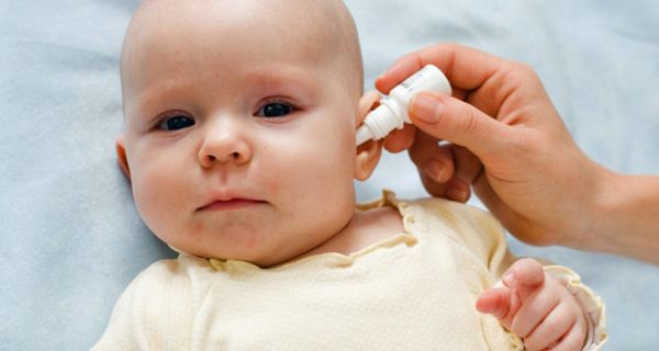 Baby bekommt von einer Hand Tropfen ins Ohr geträufelt