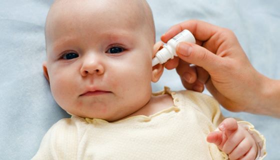 Baby bekommt von einer Hand Tropfen ins Ohr geträufelt