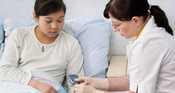 Krankenhausszene: Junge Patientin (asiatisch aussehend) bekommt von älterer Schwester oder Ärztin Blutzucker gemessen
