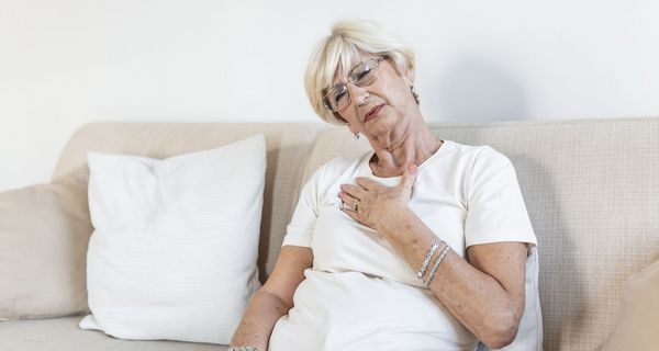 Frau, sitzt auf dem Sofa und fasst sich an die Brust.