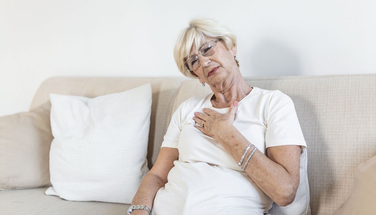 Frau, sitzt auf dem Sofa und fasst sich an die Brust.