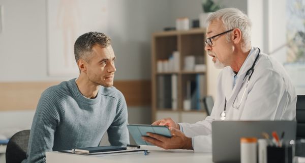 Ein Arzt erklärt einem Patienten etwas mithilfe seines Tablets.