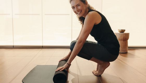 Lächelnde Frau in Sportkleidung rollt ihre Matte auf.