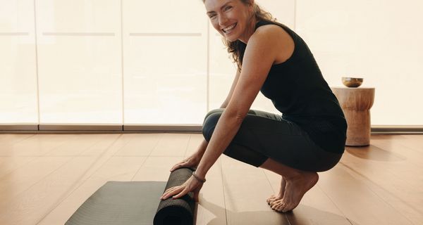Lächelnde Frau in Sportkleidung rollt ihre Matte auf.