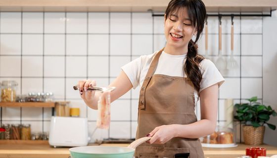 Junge Frau legt einen Streifen Bacon in eine Pfanne.