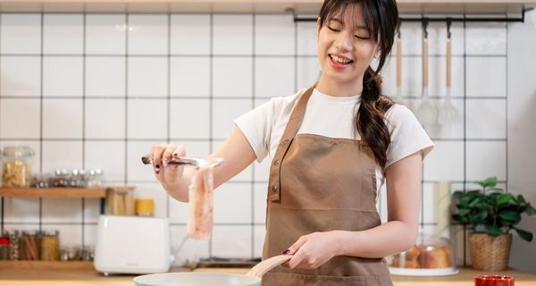 Junge Frau legt einen Streifen Bacon in eine Pfanne.