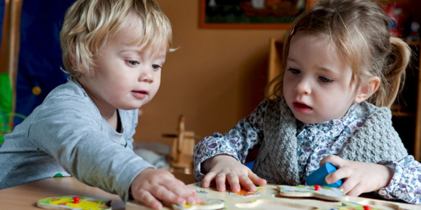 Zwei ca. 3-jährige Kinder puzzlen an einem Tisch