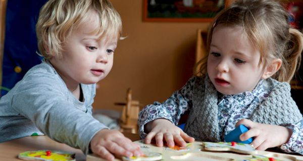 Zwei ca. 3-jährige Kinder puzzlen an einem Tisch