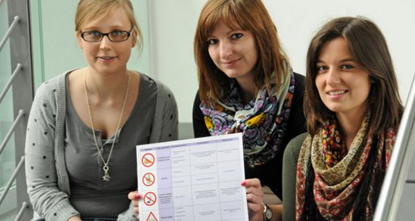 Drei Pharmaziestudentinnen zeigen ein Poster.