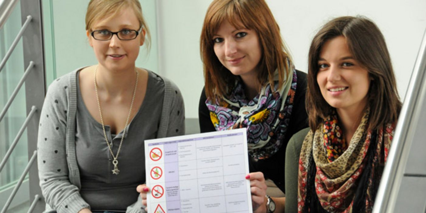 Drei Pharmaziestudentinnen zeigen ein Poster.