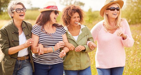 Gruppe von vier lachenden Frauen in der Natur unterwegs.