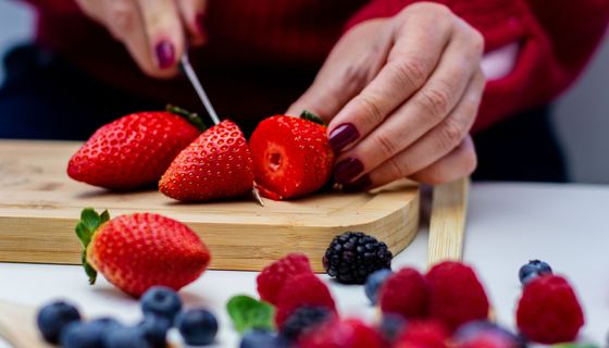 Nahaufnahme von weiblichen Händen, die Erbeeren auf einem Brettchen schneiden.