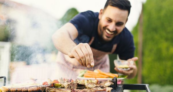 Mann, würzt sein Fleisch auf dem Grill.