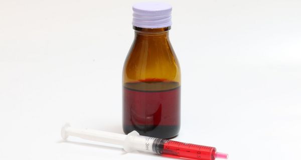 Eine, mit roter Flüssigkeit gefüllte, Pipette liegt vor weißem Hintergrund neben einer Braunglasflasche.