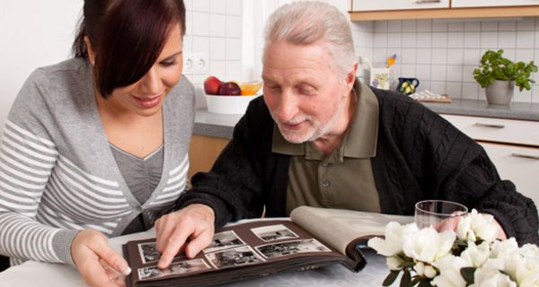Junge Frau mit älterem Mann am Küchentisch beim Betrachten eines Fotoalbums