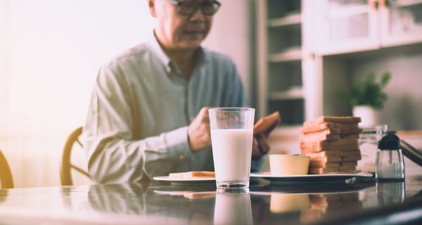 Senior, am Frühstückstisch mit einem Glas Milch.