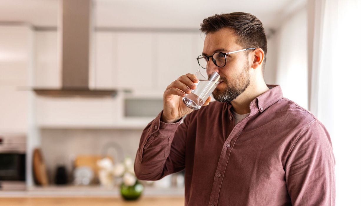 Junger Mann trinkt ein Glas Wasser.