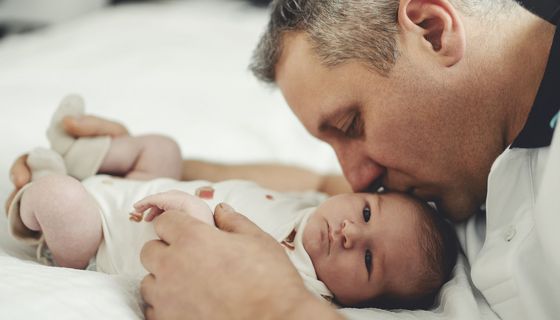 Mann mit grauen Schläfen küsst ein kleines Baby auf den Kopf.